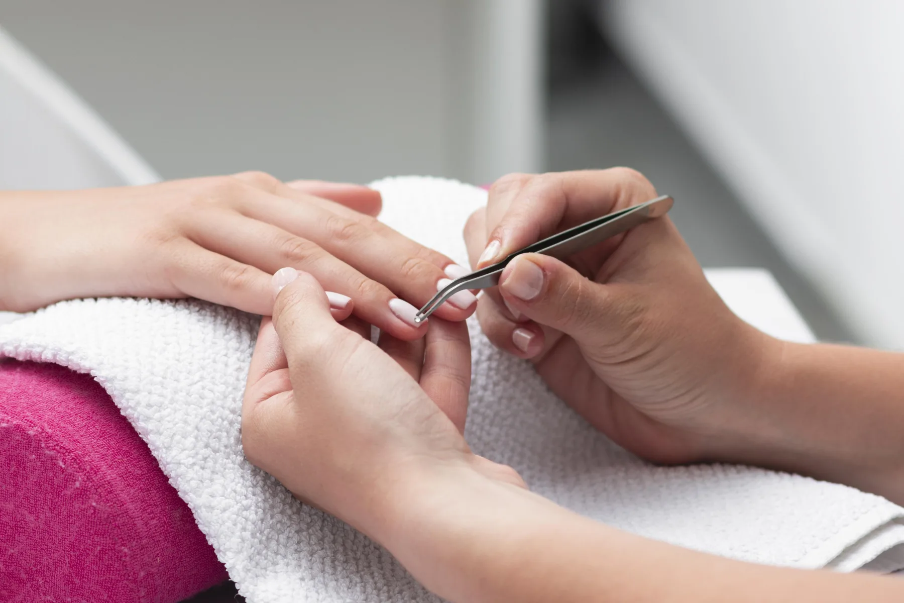 Nail technician using tweezers to place a tip on a client's finger during an extension appointment